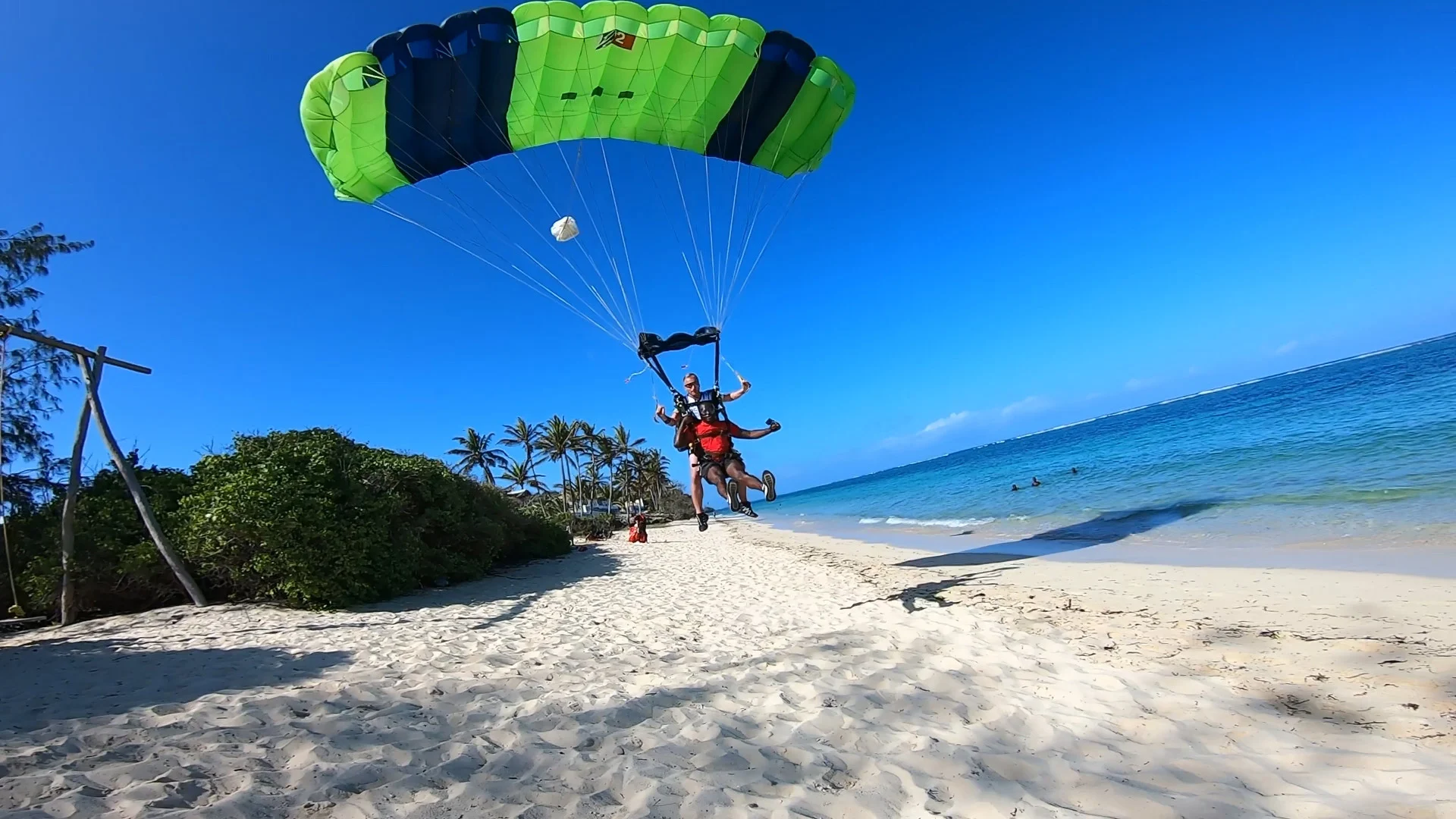 Tandem skydivers landing on the white sands of Diani Beach under a parachute